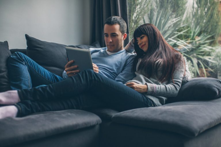 Young Couple Lying On The Sofa And Browsing Tablet Computer